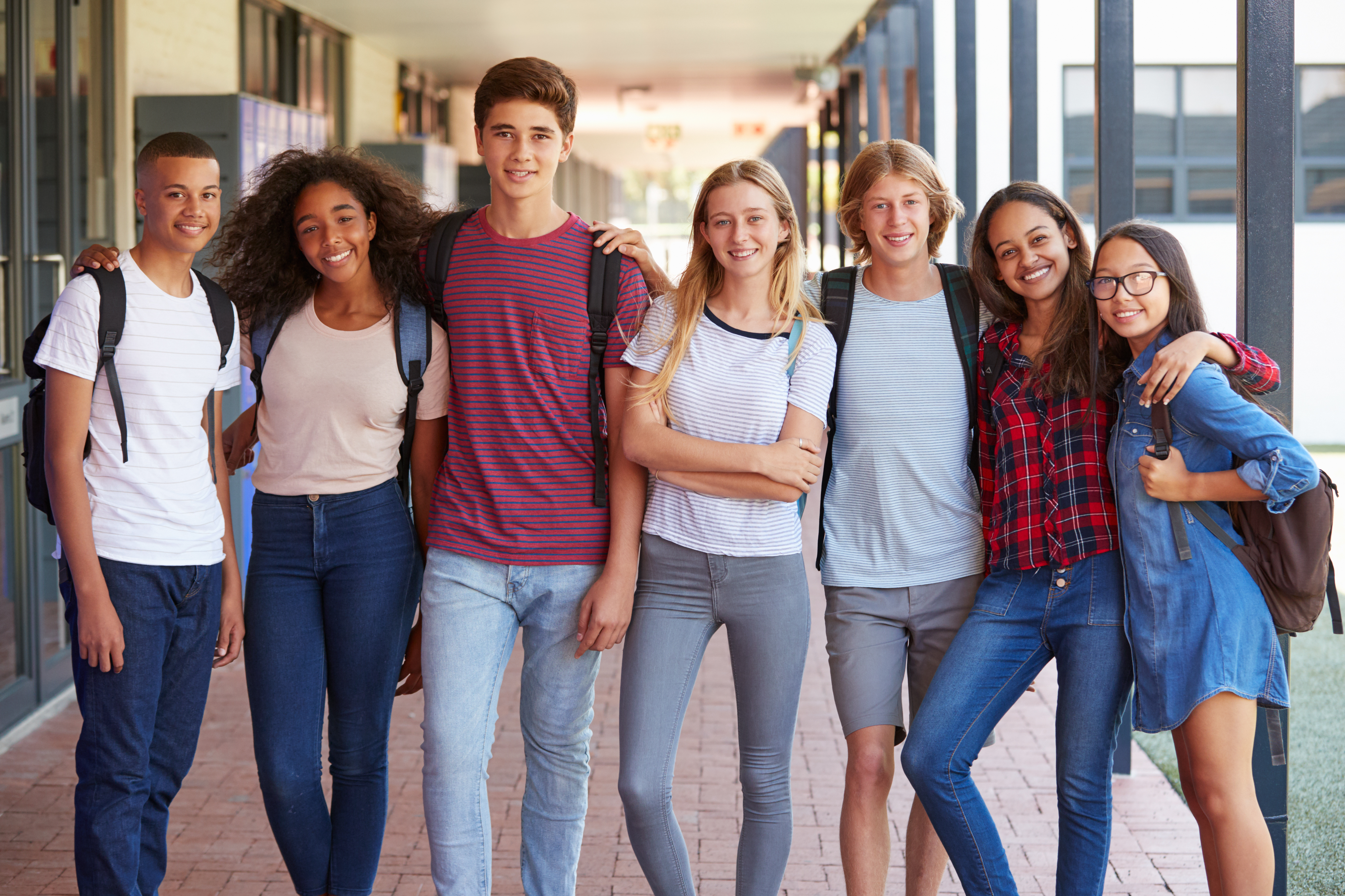 A diverse group of smiling high-school students standing together in a school hallway